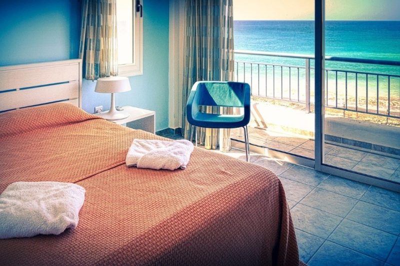 Image of a hotel bed with an open patio door overlooking the ocean.